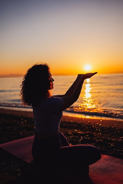 Foto jovem segurando o sol nas mãos meditando perto do mar