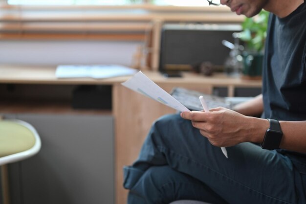 Jovem segurando tablet digital e lendo documento no sofá