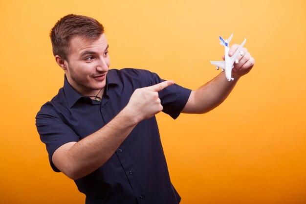 Jovem segurando um avião de brinquedo na camisa azul sobre fundo amarelo. As aventuras ainda estão por vir