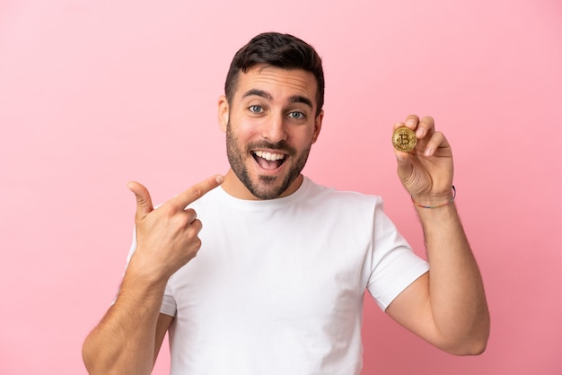 Jovem segurando um Bitcoin isolado em um fundo rosa e fazendo um gesto de polegar para cima