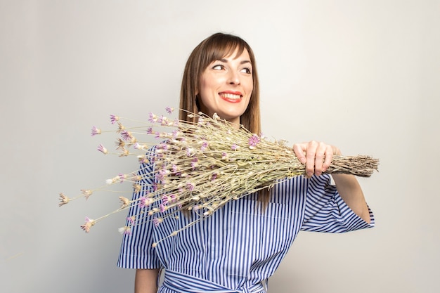 Jovem segurando um buquê de flores silvestres, uma garota mostra emoção em uma superfície clara