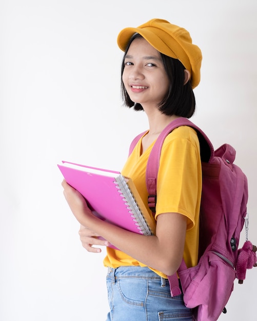 Jovem segurando um caderno rosa e usando um chapéu amarelo com mochila