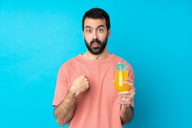 Jovem, segurando um cocktail sobre azul apontando para si mesmo