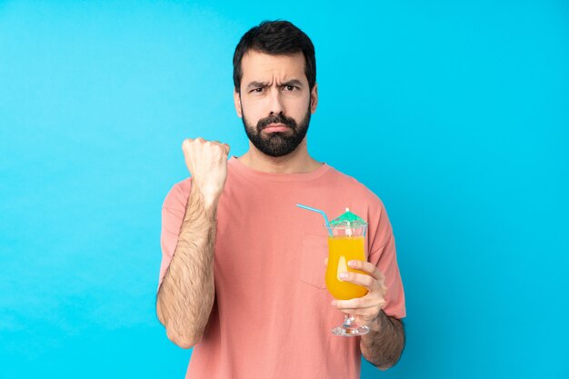 Jovem, segurando um cocktail sobre parede azul isolada com gesto de raiva