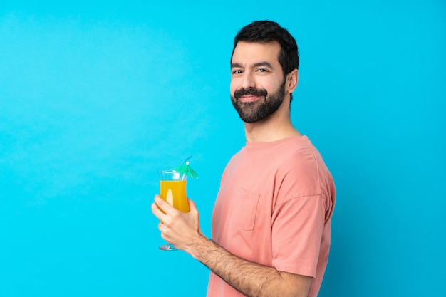 Jovem segurando um cocktail sobre parede azul isolada com os braços cruzados e olhando para a frente