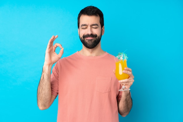 Jovem, segurando um cocktail sobre parede azul isolada em pose de zen