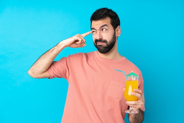 Foto jovem segurando um cocktail sobre parede azul isolada, fazendo o gesto de loucura, colocando o dedo na cabeça