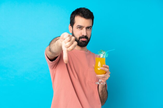 Jovem, segurando um cocktail sobre parede azul isolada, mostrando o polegar para baixo com expressão negativa