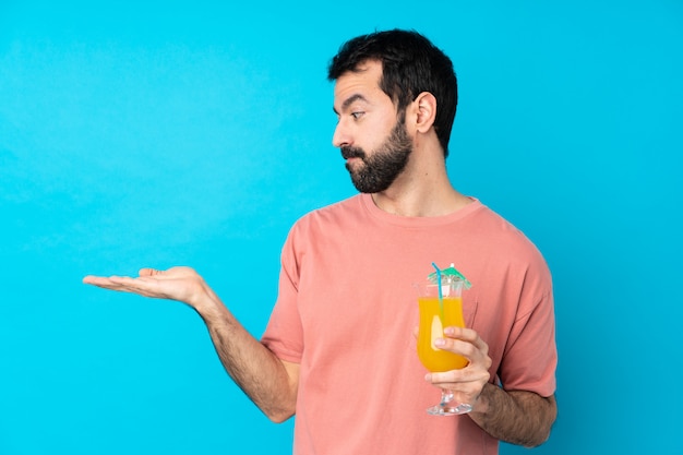 Jovem segurando um cocktail sobre parede azul isolada segurando copyspace com dúvidas