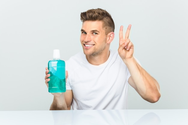 Jovem, segurando um colutório mostrando sinal de vitória e sorrindo amplamente.