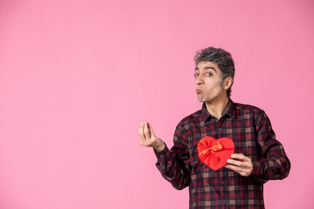 Jovem segurando um coração vermelho em forma de presente na parede rosa