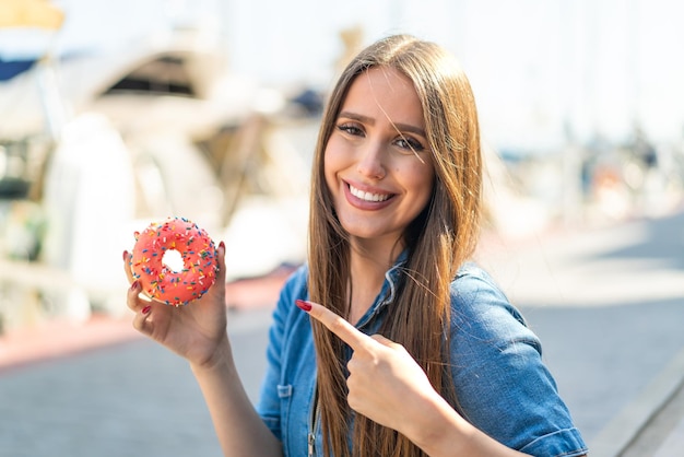 Foto jovem segurando um donut ao ar livre e apontando-o