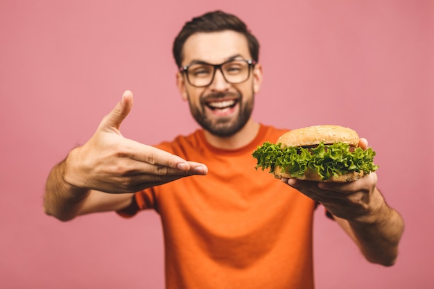 Jovem, segurando um pedaço de hambúrguer. o aluno come fast-food. cara com muita fome.