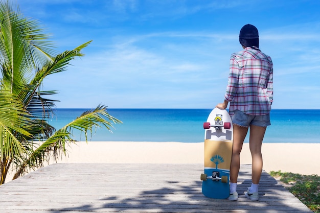 Jovem segurando um skate da velha guarda e em pé ao lado de uma praia