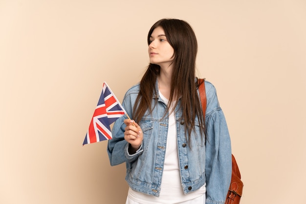 Jovem segurando uma bandeira do Reino Unido isolada em um lado bege