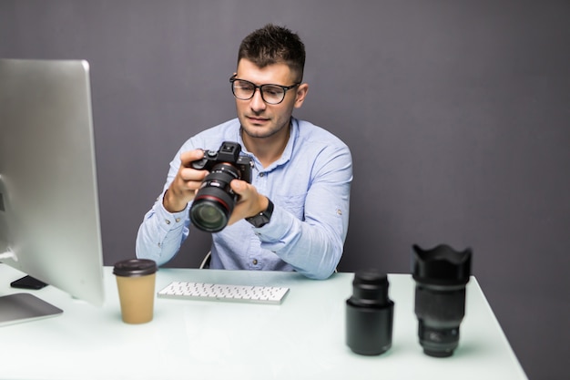 Foto jovem segurando uma câmera digital e sorrindo enquanto está sentado em seu local de trabalho