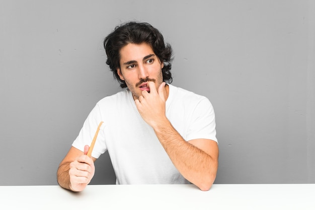 Jovem segurando uma escova de dentes relaxado pensando em algo olhando para um espaço de cópia.