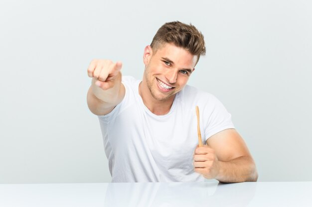 Jovem, segurando uma escova de dentes, sorrisos alegres, apontando para a frente