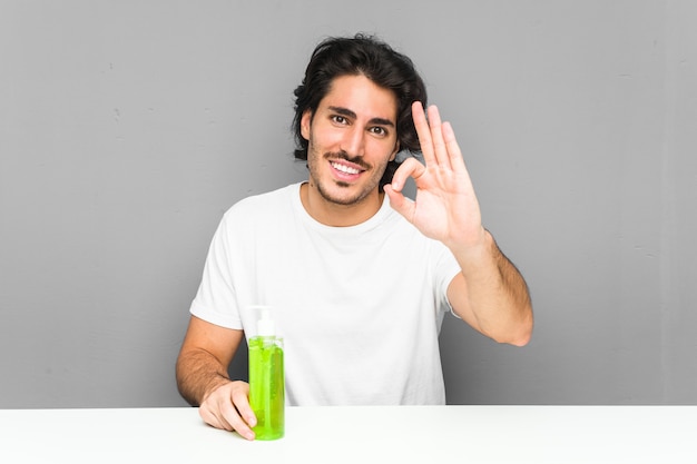 Jovem, segurando uma garrafa de aloe vera alegre e confiante mostrando o gesto de ok.