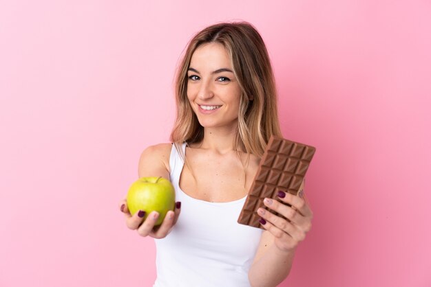 Jovem, segurando uma maçã e chocolate sobre parede isolada