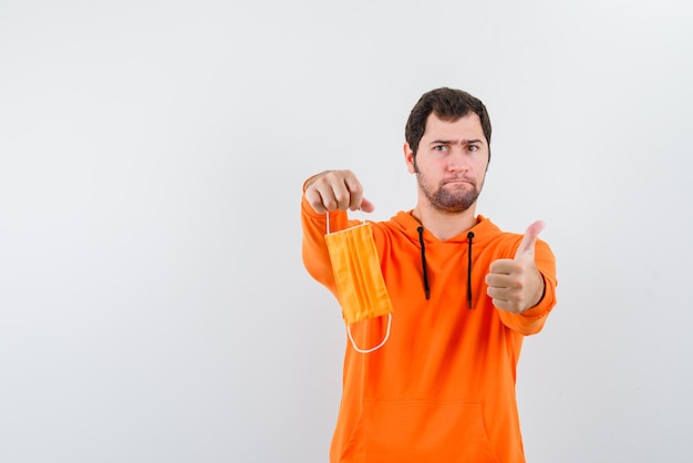 Jovem segurando uma máscara na mão e mostrando um sinal de mão OK no fundo branco