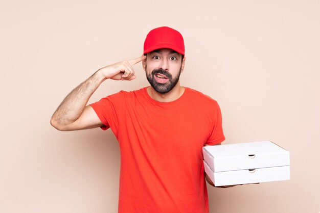 Jovem, segurando uma pizza sobre fundo isolado, fazendo o gesto de loucura, colocando o dedo na cabeça