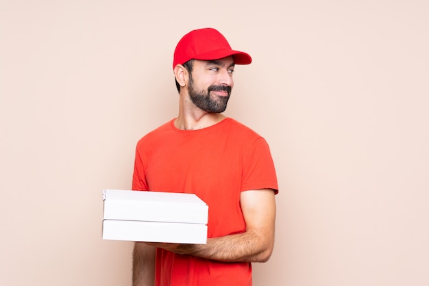 Jovem, segurando uma pizza sobre parede isolada com os braços cruzados e feliz