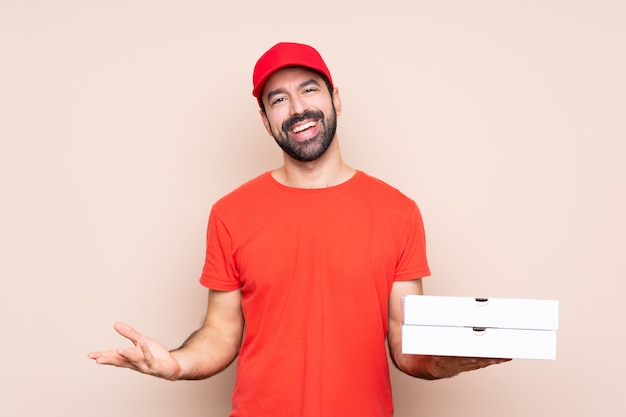 Jovem, segurando uma pizza sobre parede isolada sorrindo