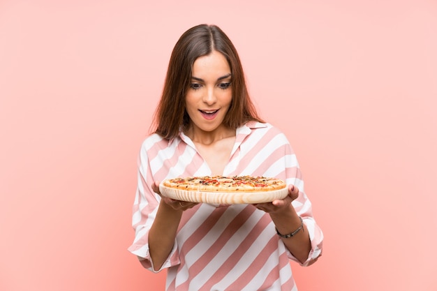 Jovem, segurando uma pizza sobre parede rosa isolada