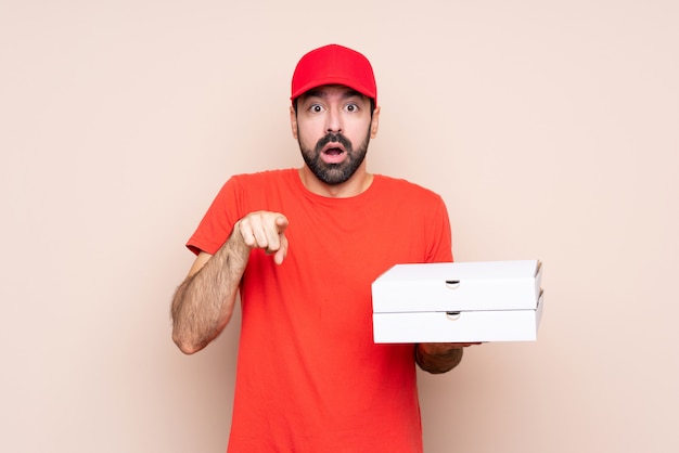 Jovem, segurando uma pizza surpreso e apontando a frente