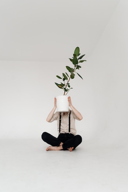 Foto jovem segurando uma planta em vaso enquanto está sentado contra um fundo branco