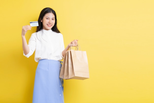 Jovem segurando uma sacola de compras com uma cara feliz. Mão segurando um cartão de crédito sobre o fundo amarelo