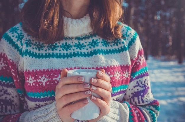 Jovem segurando uma xícara de café com marshmallow na floresta de inverno