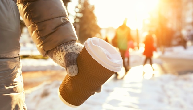 Jovem segurando uma xícara de café para viagem no parque de inverno