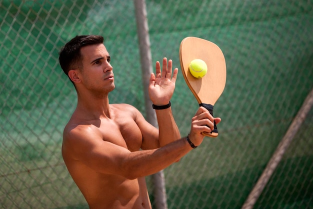 Foto jovem sem camisa jogando tênis enquanto está de pé contra a cerca de cadeia