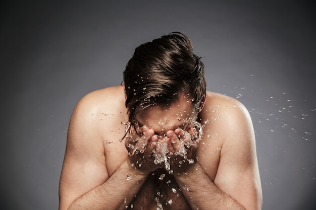 Jovem sem camisa retrato lavando o rosto com água