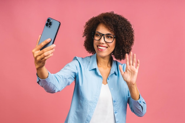 Jovem senhora casual afro-americana engraçada fazendo careta e fazendo selfie em smartphone isolado sobre fundo rosa