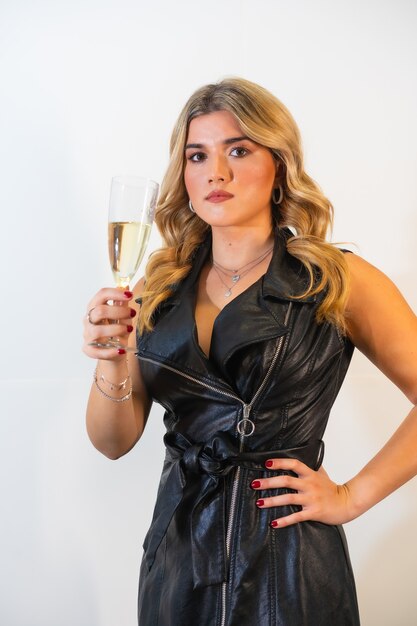 Jovem senhora de cabelos louros em um vestido preto elegante posando com uma taça de champanhe