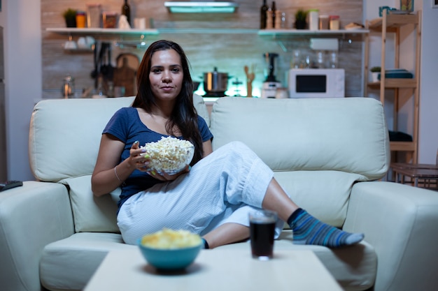 Foto jovem senhora de pijama assistindo tv na sala de estar sentada no sofá