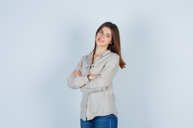 Jovem senhora em jeans casual, mantendo as mãos cruzadas e olhando alegre, vista frontal.