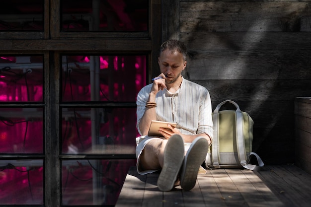 Jovem senta-se em escadas de madeira ao ar livre escrevendo notas em bloco de papel em raios de sol