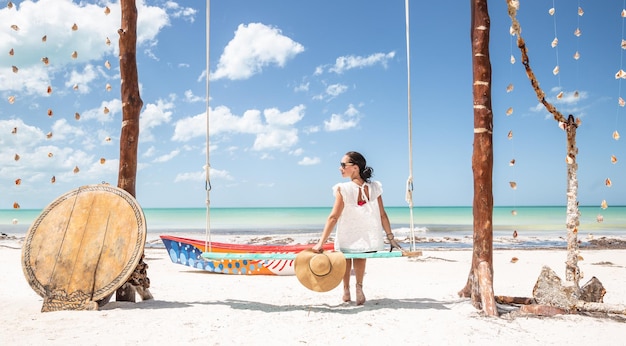 Jovem senta-se em um grande balanço sozinha em um paraíso tropical durante as férias segurando o chapéu de sol na mão