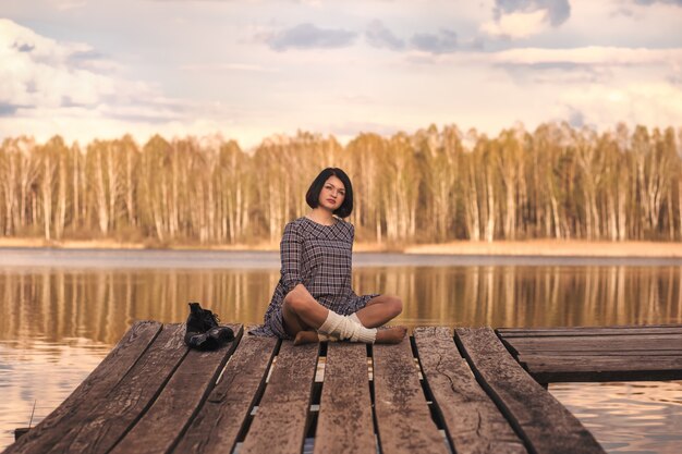 Jovem senta-se em um píer em um vestido de verão