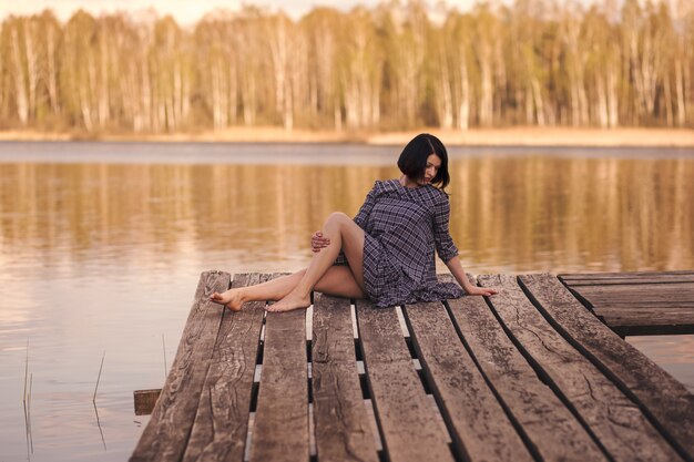 Jovem senta-se em um píer em um vestido de verão