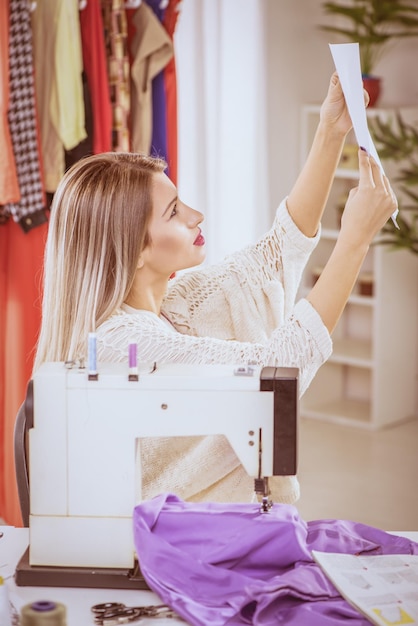 Jovem senta-se na frente da máquina de costura e olhando esboços de roupas.