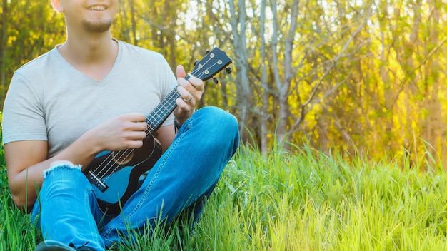 Jovem senta-se na grama tocando ukulele