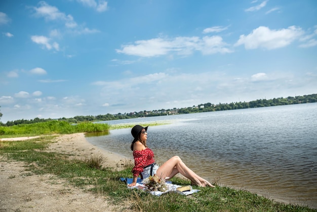 Jovem senta-se perto da lagoa e descansa desfruta de um dia quente de verão na natureza
