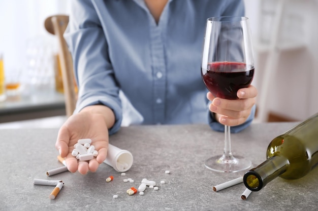 Jovem sentada à mesa com pílulas de álcool e cigarros conceito de maus hábitos