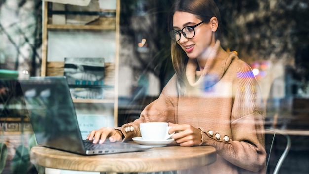 Foto jovem sentada à mesa de café e trabalhando no laptop