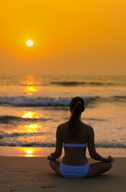 Jovem sentada em posição de lótus na praia do pôr do sol